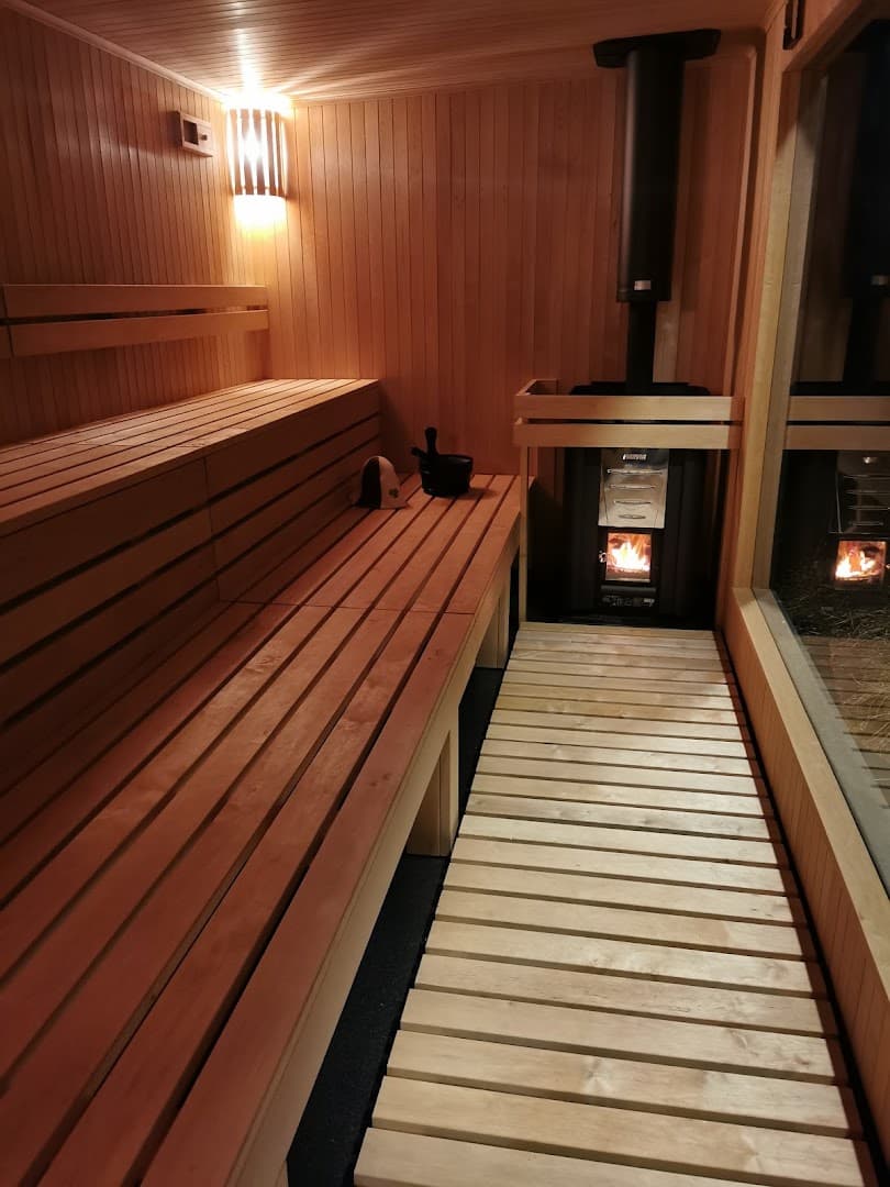 Wooden sauna interior featuring wooden benches, slatted floor panels, and a wood-burning stove with a glowing fire.